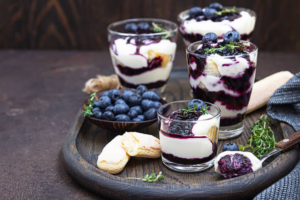 Dessert from mascarpone or ricotta cheese, blueberries and biscuit in glass on a dark background. No baked cheesecake or tiramisu. Dessert from mascarpone or ricotta cheese, blueberries and biscuit in glass on a dark concrete background. No baked cheesecake or tiramisu. yogurt fruit biscotti berry fruit stock pictures, royalty-free photos & images