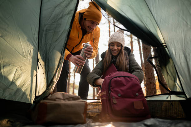 istock Young couple taking insulated drink container from backpack while crouching in front of tent 1287609222