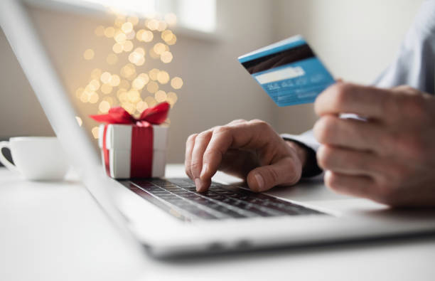 compras en línea durante las vacaciones. hombre ordenando regalo de navidad usando computadora portátil y tarjeta de crédito - holiday fotografías e imágenes de stock