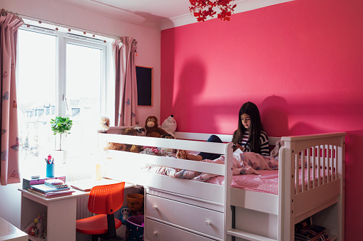 A little girl sitting in her princess pink bedroom in the North East of England engrossed in her phone on her elevated bunk bed chatting with friends using her mobile phone.