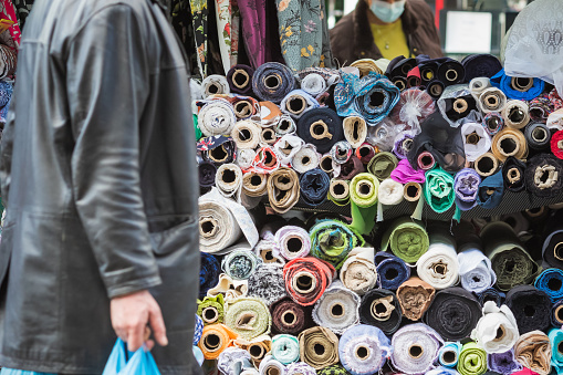 Rolls of textile fabric displayed for sale at Walthamstow market in London, with a shopper passing by