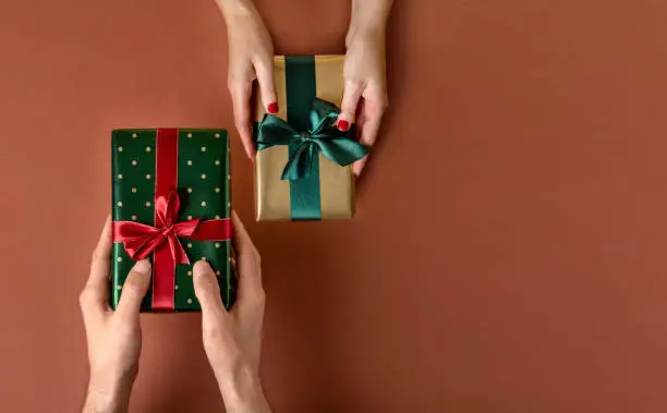 Photo of Woman giving her boyfriend a wrapped Christmas gift.Christmas giftboxes with tidewater green ribbon. Hands Giving Gifts Close-up.