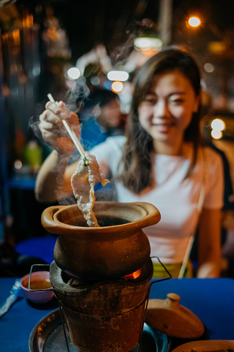 Young asian woman tourist eating Thai style Jim Jum hotpot at Bangkok street during night time