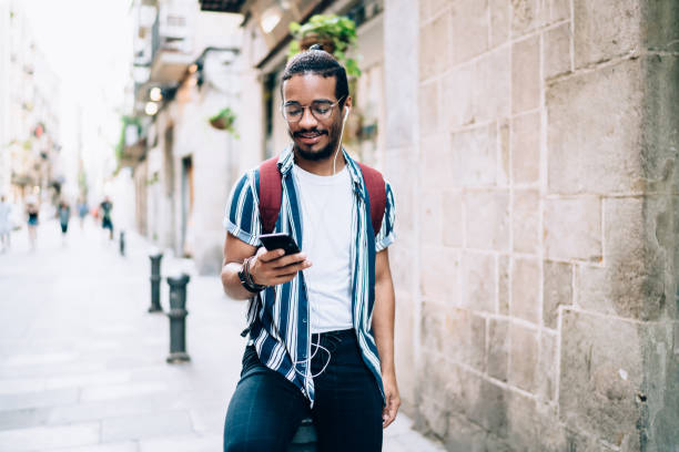 istock Cheerful man with earphones using smartphone on street 1287619566