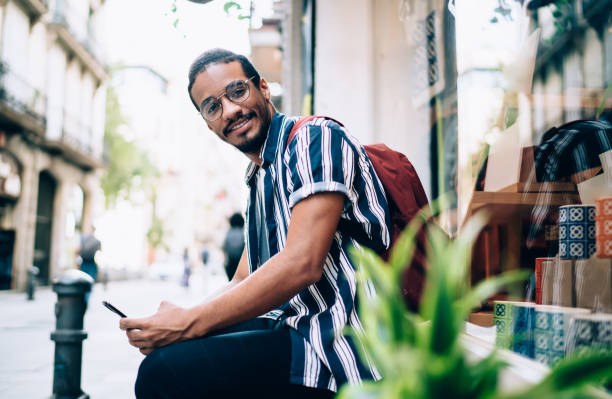 istock Half length portrait of smiling dark skinned male millennial using smartphone communicating and browsing on free time, smiling african american looking at camera satisfied with 4G connection on street 1287619567