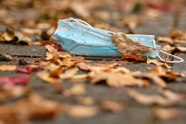 Thrown away dirty disposable face mask lying on ground stock photo