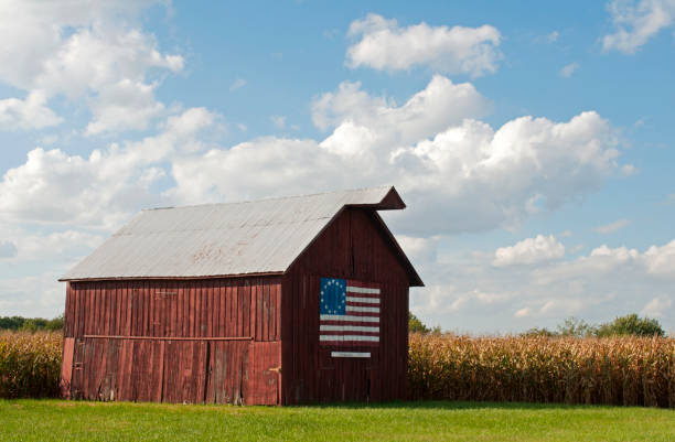 Nilwood, IL, USA, Oct. 1, 2019: A weathered wooden barn with a painting of the 13-star Betsy Ross flag (an early American flag design) stands near cornfields along old Route 66 in Nilwood.