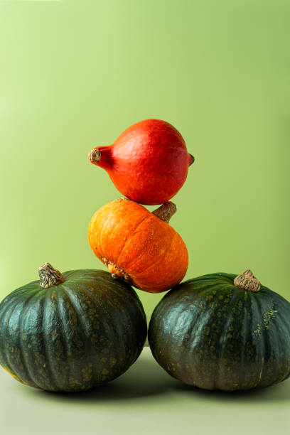 istock Stacked green and orange pumpkins on lime green background 1287625296