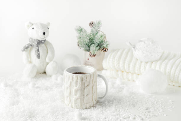Winter themed stilllife with mug of tea, knitted teddy bear, white decor on white background