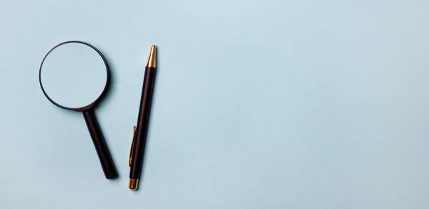 istock On a light blue background, a magnifying glass and a pen. View from above. Place to insert text or illustrations 1287626527