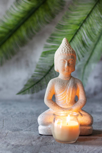 istock Buddha figure in meditation with burning candle on grey concrete background with palm leaf 1287626555