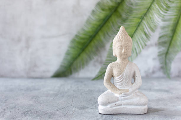 istock Buddha figure in meditation on grey concrete background with palm leaf. 1287626570