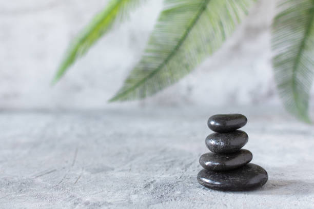 istock Black zen stones in a stack on grey concrete background with palm leaf. 1287626591