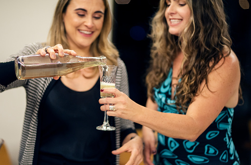 Smiling woman pouring her friend a glass of sparkling wine during an after work party