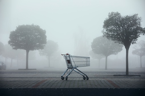 Abandoned shopping cart on parking lot in thick fog. Themes shopping, financial crisis and gloomy weather.