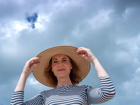 Mature woman with beach hat in the background the sea, low angle view