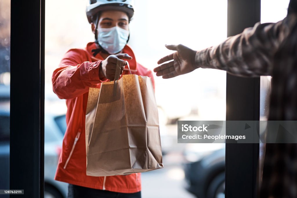 We've got you covered during lockdown Shot of a masked man delivering a food package Delivering Stock Photo