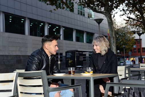 Two young friends talking and having a drink on the terrace of a bar