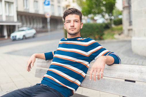 Young man sitting on bench. Handsome guy, outdoors
