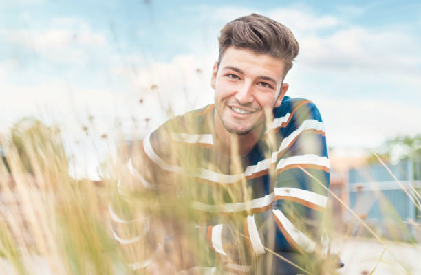 Beautiful guy showing white teeth smiling to camera through blurred grass