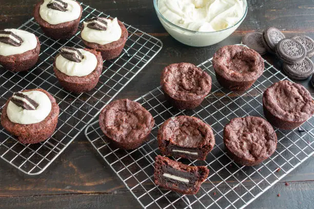 Brownie cups filled with a sandwich cookie and topped with frosting on a wire cooling rack