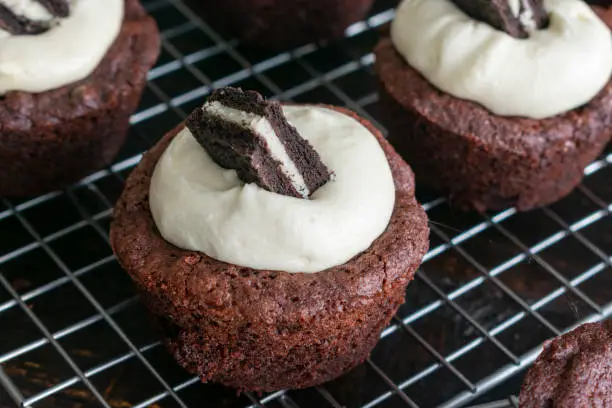 Brownie cups filled with a sandwich cookie and topped with frosting on a wire cooling rack