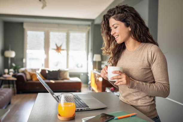 istock Beautiful woman is using laptop and drinking coffee at home 1287639968