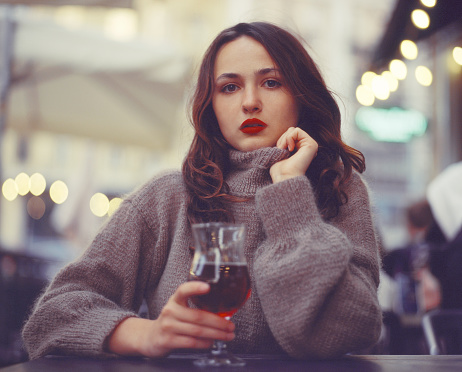 Young Caucasian woman with red lipstick drinking wine on a terrace