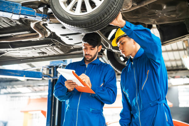 istock Mechanic in blue work wear uniform inspects the car bottom with his assistant. Automobile repairing service, Professional occupation teamwork. Vehicle maintenance. 1287641275