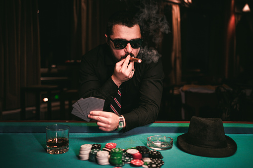 Young caucasian man playing poker and smoking a cigar in a casino