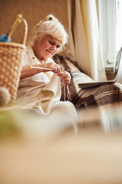 istock Nice old woman knitting and using notebook at home 1287649222