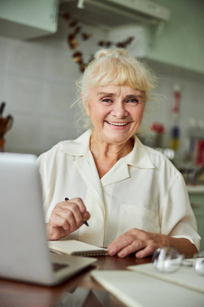 istock Cheerful old woman using notebook and taking notes at home 1287649288