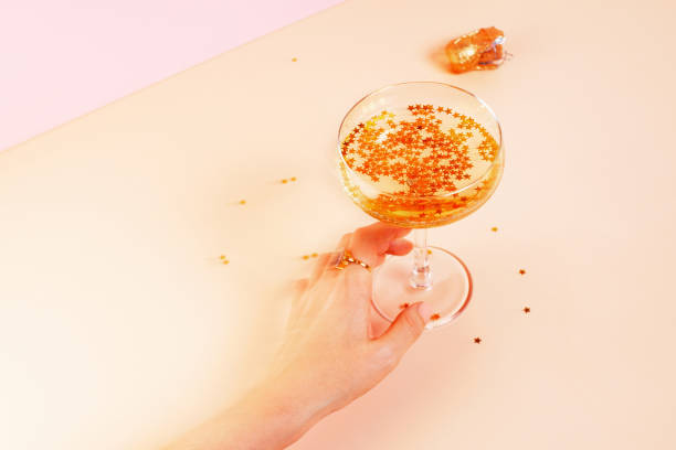 kieliszek szampana, kobieta"u2019s ręka i złote gwiazdy konfetti na żółtym tle - champagne pink luxury table zdjęcia i obrazy z banku zdjęć