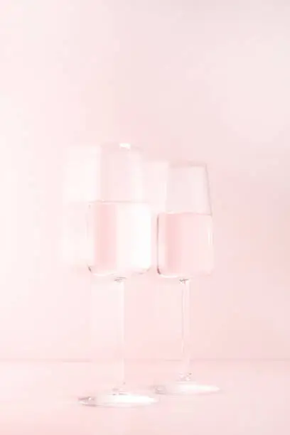 Two glasses of champagne or wine on the pink background, creative festive composition, concept of alcoholic intoxication
