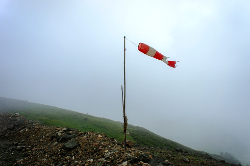 Old striped red-white windsock, indicator of the strength and direction of the wind in the Caucasus mountains in the fog, Aibga ridge, hike, trekking, travel