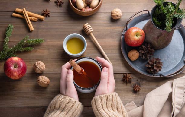 istock Hands keep  mug of  aroma  Christmas Apple tea with cinnamon on a wooden table 1287656418