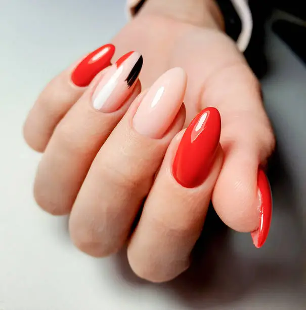 Bright red gel Polish with camouflage design and brushstrokes. A woman's hand with long almond-shaped nails and a multi-colored design.