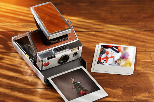 Vintage instant film camera and some printed christmas ornament photographs on wooden table under afternoon sunlight