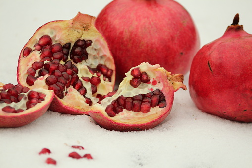 One broken ripe pomegranate with bright red grains close-up and two whole pomegranate fruits on the snow outdoors in winter.