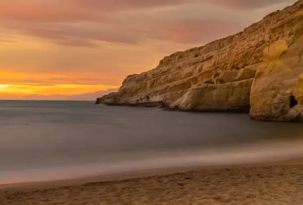 Photo of Sunset next to the roman catacombs carved on the sandstone cliffs above the Matala Beach, Crete, Greece. In Roman times, the dead were buried in them, later they were used by the first Christians