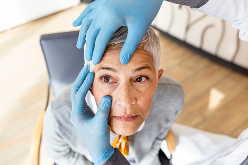 Mature Doctor examining senior woman eyes in his office