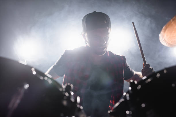 istock Rock band musician with drumstick playing drums with smoke and backlit on background 1287685433