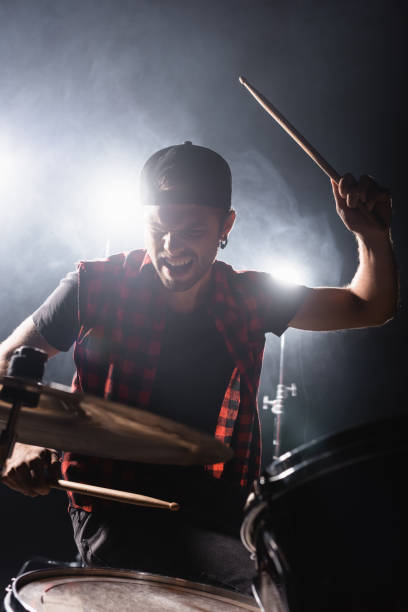 istock Rock band drummer holding drumstick and playing drums with back light and smoke on background 1287685441