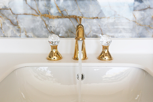 Close up shot of a vintage two handle faucet in a bathroom with marble textured tiles. Copper retro styled water mixer. Copy space, background