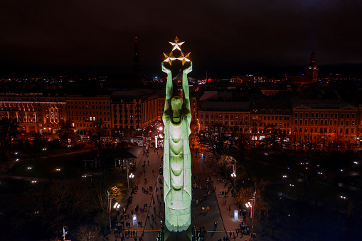 Monument of freedom at night in Riga, Latvia during Staro Riga event. Milda - Statue of liberty holding three stars over the city illuminated in different colors.