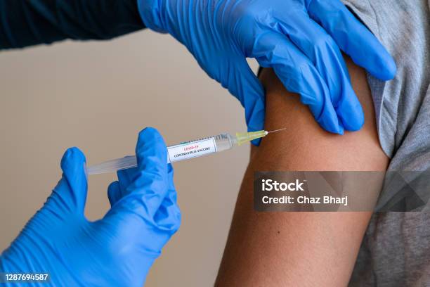 Female Doctor Wearing Blue Latex Gloves Injecting A Child In Her Arm With A Needle And Syringe Containing A Dose Of The Covid19 Vaccine Cure By Way Of Immunisation 052 Stock Photo - Download Image Now