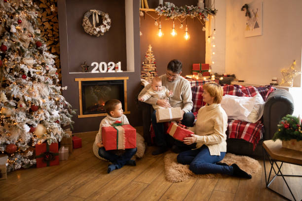 Family Opening Christmas Presents near Christmas tree in decorated home, Happy New year 2021 Family Opening Christmas Presents near Christmas tree in modern decorated home, Happy New year 2021 6 9 months stock pictures, royalty-free photos & images