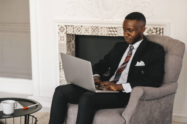 istock Handsome Afro American businessman in classic suit is using a laptop and smiling while working in modern office 1287696079
