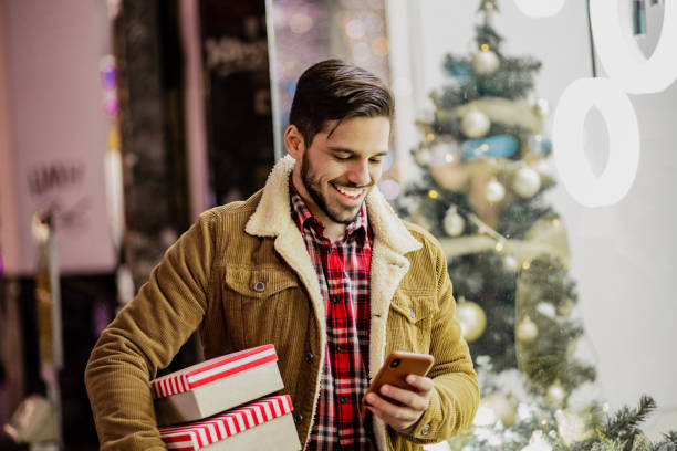 istock Young man in Christmas shopping holding presents and using mobile phone 1287697255