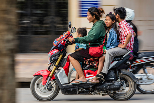 A mother transporting her three children home from school on her scooter, through Battambang, Cambodia. Scooters are a common form of transport throughout Cambodia.